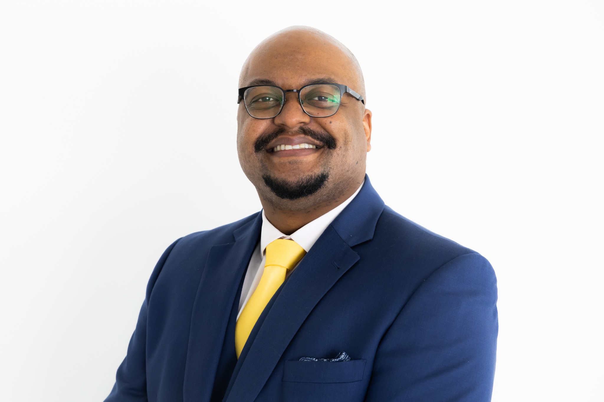 Rev. Diondre McBride smiling, wearing a navy suit and yellow tie.